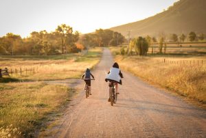 Dos niños en bicicleta por un camino de pueblo rural en el atardecer de verano