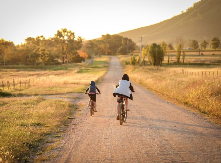 Dos niños en bicicleta por un camino de pueblo rural en el atardecer de verano